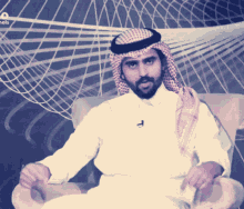 a man with a beard and a head scarf sits in a chair in front of a sign that says channel