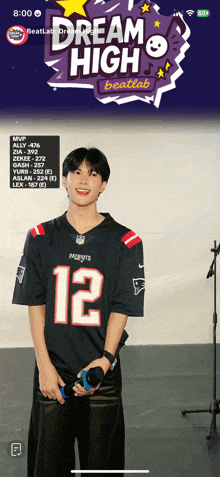 a man in a patriots jersey is holding a microphone in front of a sign that says dream high
