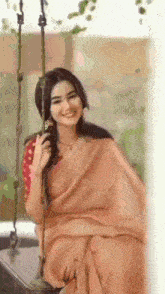 a woman in a sari is sitting on a swing and smiling