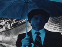 a man in a suit and tie holds a blue umbrella in the rain