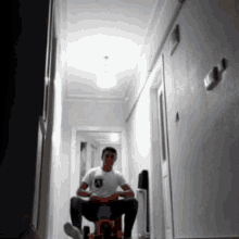 a man in a white shirt is sitting on a toy bike in a hallway