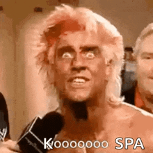 a man with pink hair is talking into a microphone while wearing a wig .