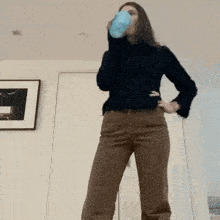 a woman is drinking from a blue cup while standing in a room .