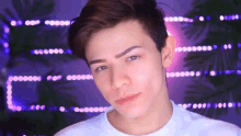 a young man wearing a white t-shirt looks at the camera