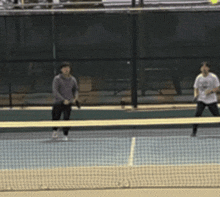 two people playing tennis on a court with a fence in the background