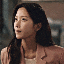 a woman wearing a pink jacket and a white shirt is looking to the side .