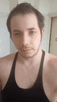a man with a beard wearing a black tank top looks at the camera