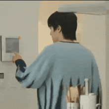 a man in a blue sweater is standing in front of a wall mounted monitor .