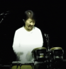 a woman in a white shirt is playing drums in the dark