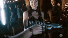 a woman in a black dress is holding a tray of shot glasses and smiling .