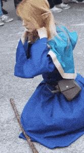 a woman in a blue dress is kneeling down with a cane