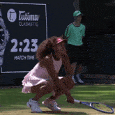 a woman is squatting down with a tennis racquet in front of an advertisement for tutima glashutte