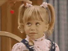 a little girl with pigtails is holding a fork in her hand and looking up .