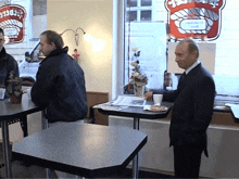 a man in a suit stands in front of a sign that says ' sandwich ' on it