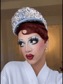 a drag queen wearing a white robe and a hat with sequins on it