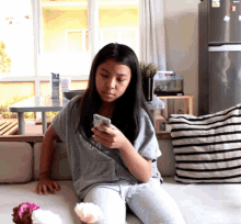 a girl is sitting on a couch looking at her cell phone