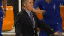 a man in a suit and tie is standing next to a man in a blue jersey .