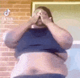a very fat man is covering his face with his hands .
