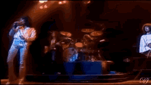 a man is singing into a microphone on a stage while another man plays drums .