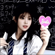 a girl in front of a blackboard holds a barbie heart