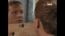 a man looking at his reflection in a mirror with tht on his hair