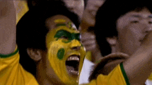 a man with yellow and green paint on his face screams