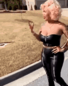 a woman with pink hair is standing on a sidewalk wearing a black top and black pants .