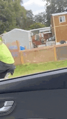 a person is sitting in a car looking out the window at a fenced in yard .