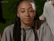 a woman with braids and hoop earrings is making a face with her eyes closed