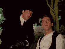 a man in a top hat looks at another man laying down