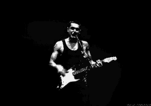 a black and white photo of a man singing into a microphone while holding a guitar .