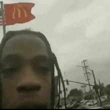a man with dreadlocks is standing in front of a red mcdonald 's flag .
