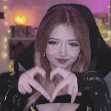 a woman is making a heart shape with her hands while sitting in a chair