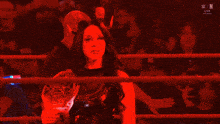 a woman is in a wrestling ring holding a trophy and giving a thumbs up