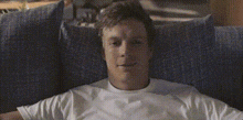 a man in a white shirt is laying on a blue couch and smiling