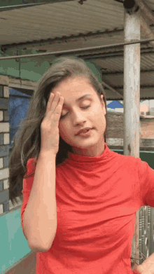 a woman in a red shirt covering her face with her hand