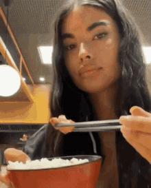 a woman is eating rice with chopsticks from a bowl in a restaurant .