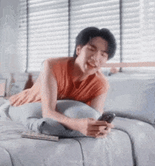 a man is laying on a bed holding a cell phone and smiling .