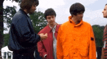 a man in an orange jacket is talking to two other men