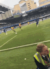 a man in a yellow vest is watching a soccer game on a field