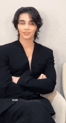 a man in a black suit is sitting on a chair with his arms crossed .