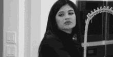 a black and white photo of a woman standing in front of a refrigerator with a hose attached to it .