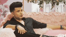 a man in a black shirt is laying on a pink fur couch