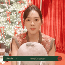 a woman holding a stuffed animal in front of a christmas tree with the words merry christmas