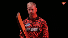 a man holding a cricket bat with the word realm on his jersey