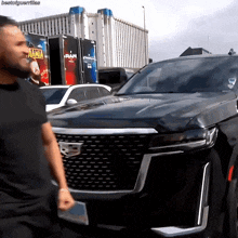 a man in a black shirt stands in front of a black car with a sign that says raw on it