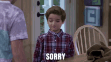 a young boy in a plaid shirt is saying sorry