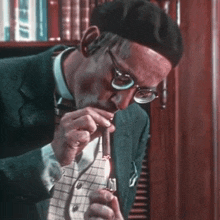 a man with glasses and a beret is lighting a cigar