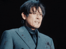 a man wearing glasses and a suit is smiling with blood on his face
