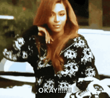 a woman in a black and white sweater is standing in front of a car and says okay